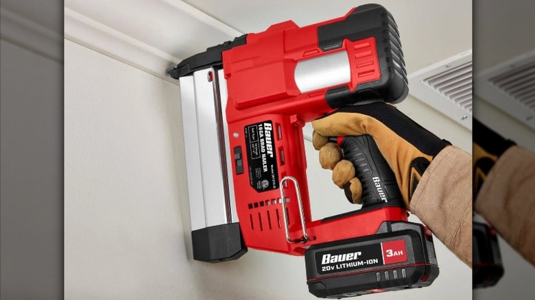 Gloved hand holding up a Bauer brad nailer up to ceiling moulding
