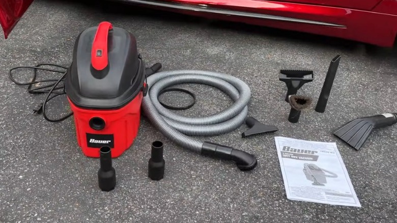 Bauer 3-gallon wet-dry vacuum with accessories on asphalt next to a red car