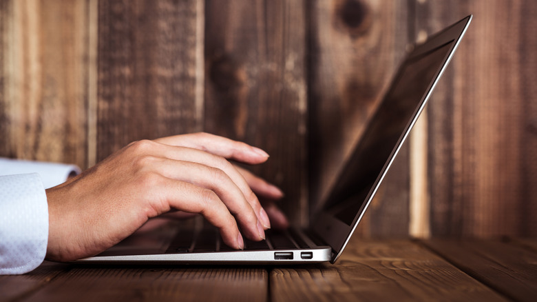 A person typing on a laptop keyboard on a table