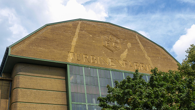 Exterior view of the historic industrial AEG Turbine Factory building with large glass windows and AEG Turbinefabrik inscribed on it.