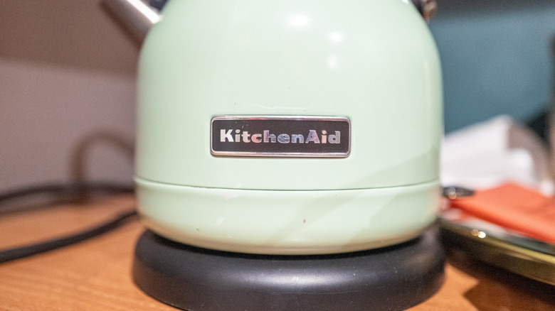 A close-up view of a light green KitchenAid electric kettle featuring the brand's metallic logo plate on its body.