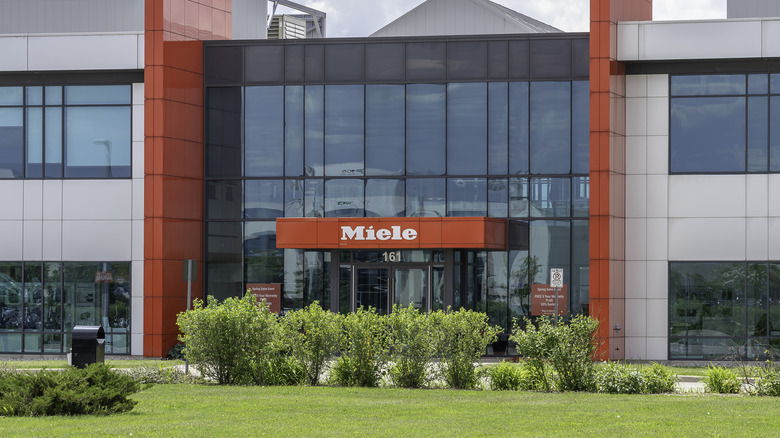 Exterior view of a modern corporate office building with glass windows and a Miele logo.