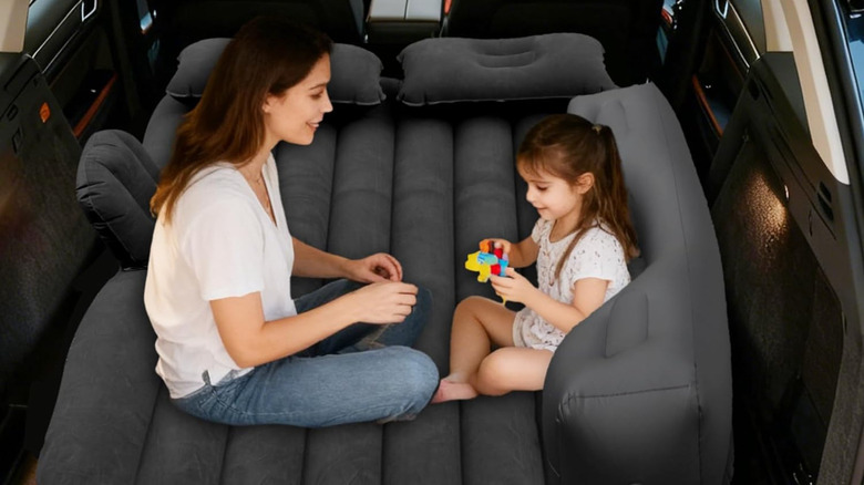 A woman and a child sitting on an inflatable bed inside a vehicle