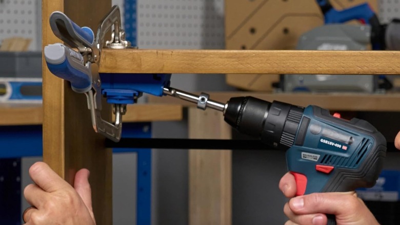 Pocket-hole jig clamped down in place while someone uses a drill on it.