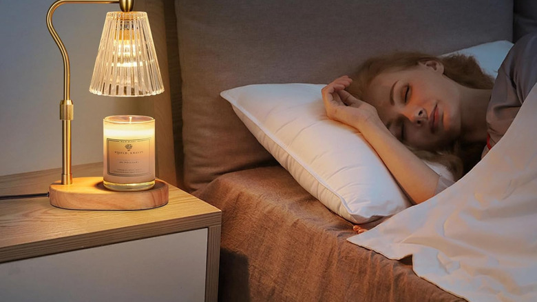 A person sleeping on a bed with a candle lamp next to them on a nightstand.