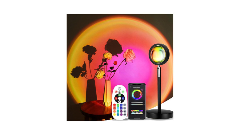 A Lekeone sunset lamp, along with its remote, illuminating a flower vase.