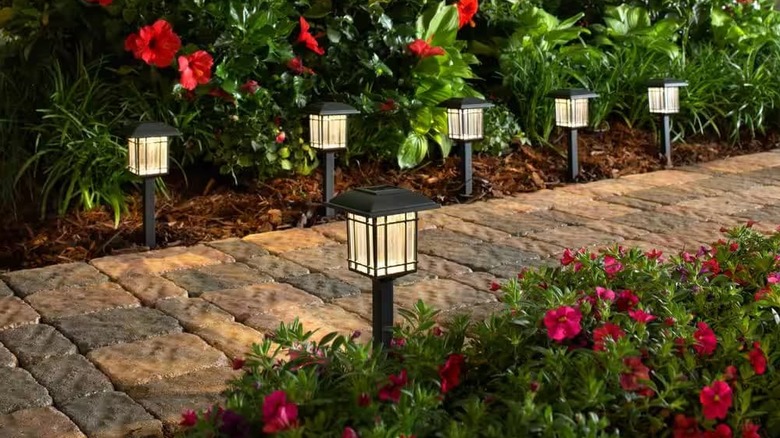 Lights lined up next to a brick sidewalk and flowers.