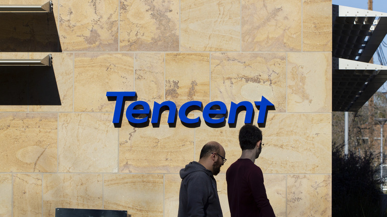 People walking past a Tencent logo on a building