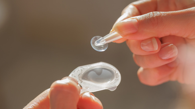 Photo of hands removing a soft contact lens from packaging.