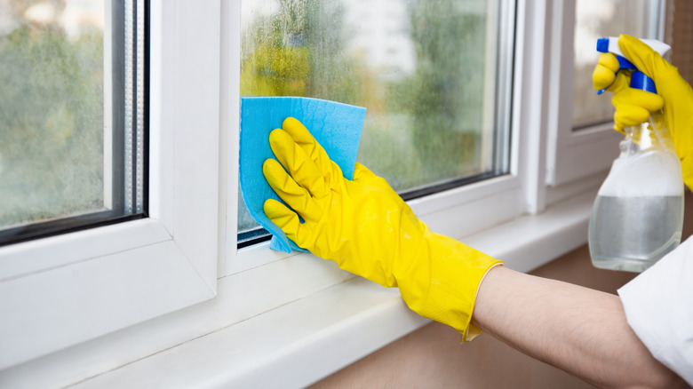 A person wearing yellow gloves cleaning the interior of a house window.