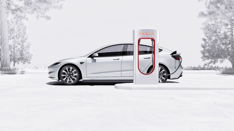 A white Tesla car is charging in a snow-covered landscape.