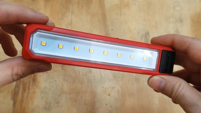 Hands holding the Milwaukee USB Rover Pocket Flood Light above a wood surface