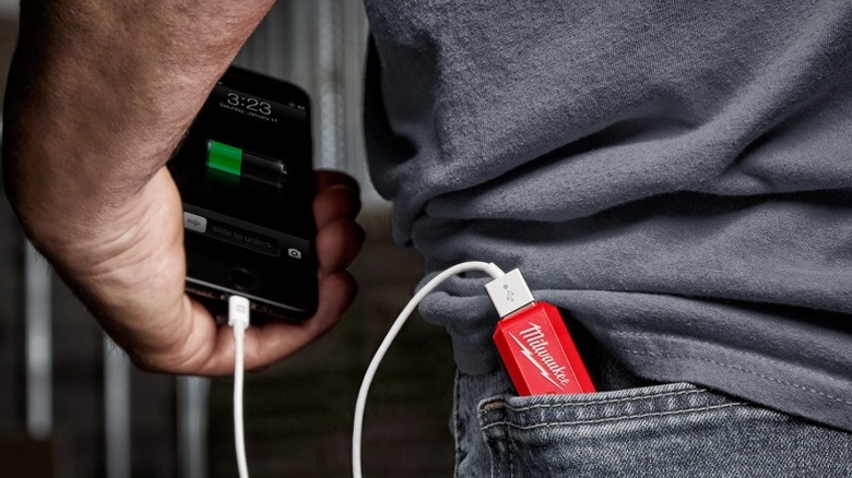 Close-up of a Milwaukee USB Charger and Portable Power Source in a person's back pocket, charging a phone