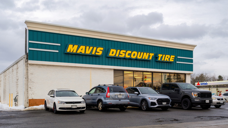 A close up overcast view of a massive Mavis Discount tire store, with the store parking lot being relatively full.