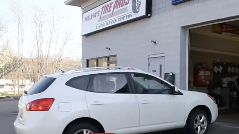 A white car rolling into the open garage at a Melvin's Tire pros auto service center in the afternoon sun.
