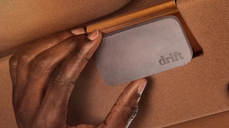 Hand touching a Drift air freshener in a brown car interior.