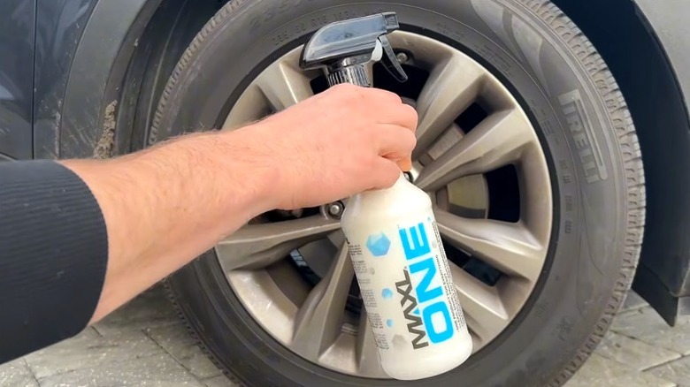 Person holding bottle of Maxl One car spray in front of a car wheel.