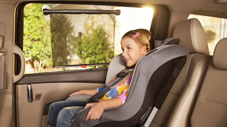 Smiling child in child seat with a Munckin Brica window shade on the passenger window.