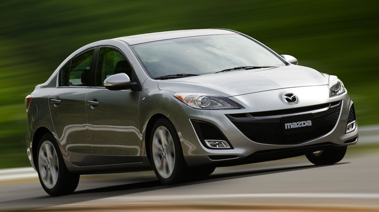 a silver 2010 Mazda 3 driving on a road in the woods