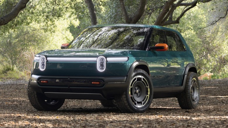 Green Rivian R3X parked in woodland.