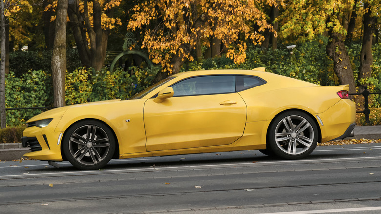 A yellow Chevrolet Camaro parked on a road near trees.
