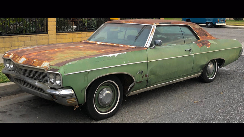 1970 Chevy Impala, covered in rust and dents, parked on the side of the road.