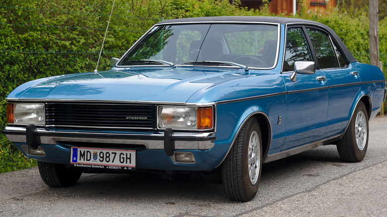 1975 Ford Granada iin blue, parked on the road with shrubbery in the background