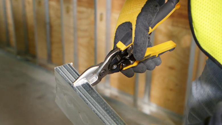 A worker wearing safety gloves using a DeWalt aviation snip on some metal flashing