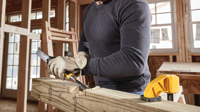 A worker wearing safety gloves using a DeWalt wood chisel on a wooden beam