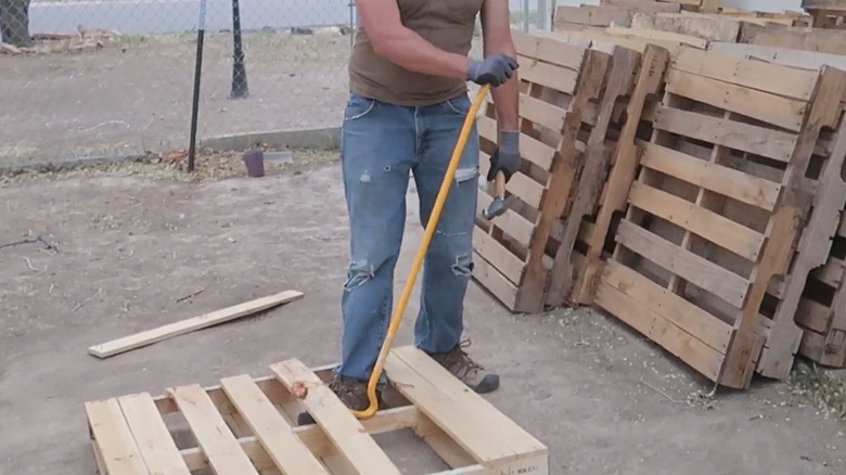 A worker wearing safety gloves using a DeWalt 42 inch wrecking bar to dismantle a wooden pallet