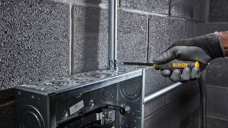 A worker wearing safety gloves using a DeWalt MaxFit screwdriver to tighten the fitting on a conduit