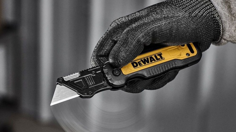 A person wearing safety gloves flicking open a DeWalt utility knife