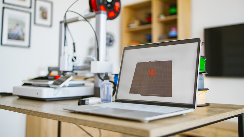 A 3D printer next to a laptop in a small office space