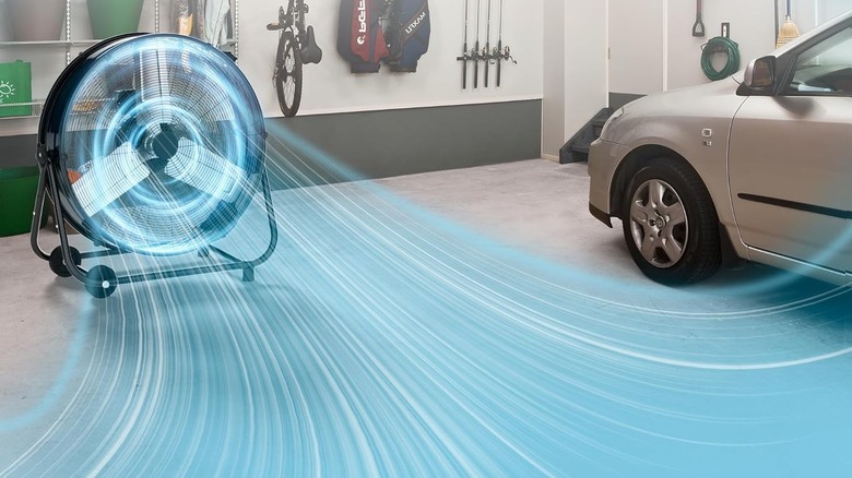A garage fan in a garage blowing near a car.