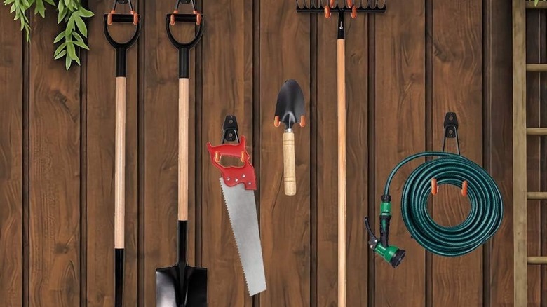 Many tools hanging from a wooden fence.