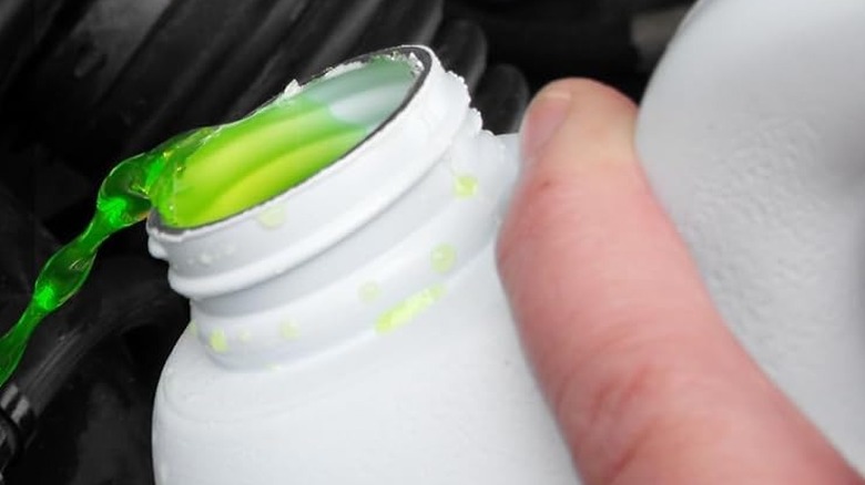 A closeup of an anti-freeze bottle being poured into a car.