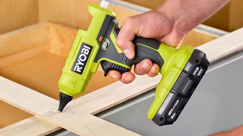 A cordless glue gun being used to flue a wooden board.