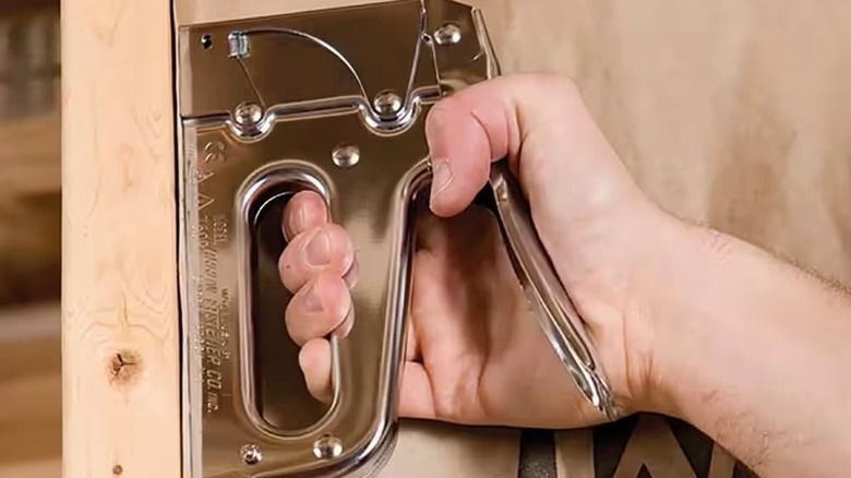 A person stapling a wood wall.