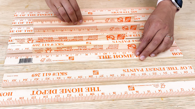A person cutting and arranging Home Depot yard sticks on a table.