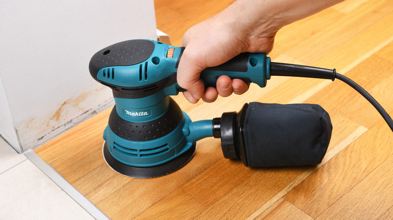 Closeup of a DIYer using a Makita BO5041 orbit sander on hardwood