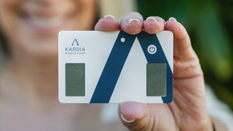 An elderly woman holding a KardiaMobile Card Personal EKG Monitor up to the camera.