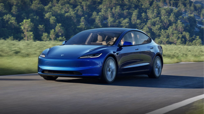 A blue Tesla Model 3 driving on a country highway