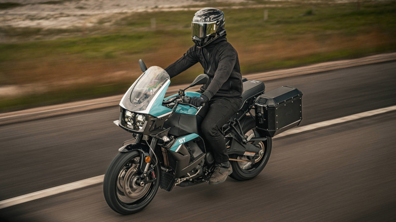 Person riding a Buell Super Touring motorcycle on a road with grass in the background