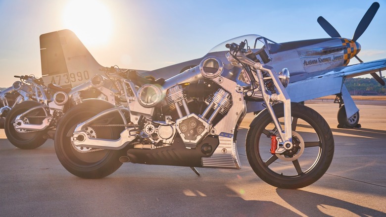 Multiple Combat Motors motorcycles parked in front of a P51 Fighter Jet with the sun setting behind them