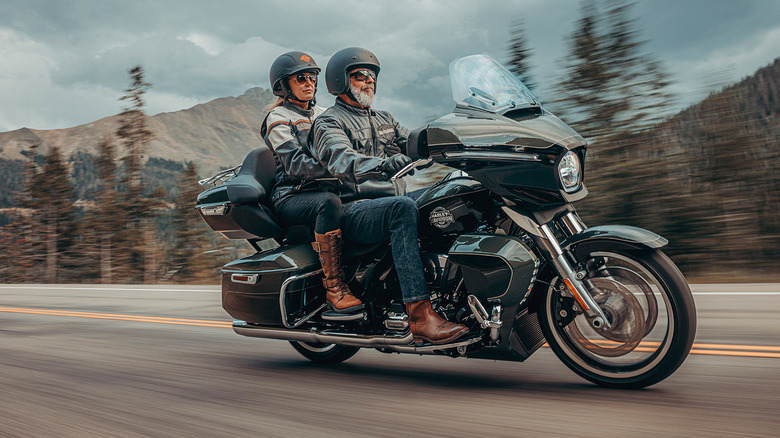 Two people riding a Harley-Davidson Street Glide on a highway with mountains and trees in the background