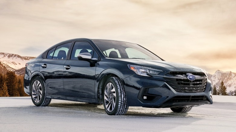 Dark blue Subaru Legacy parked on snow with mountains in the distance