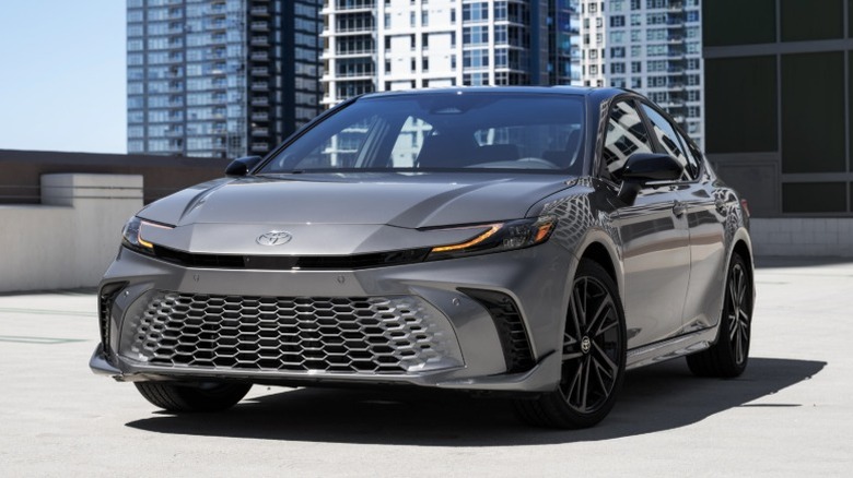 Silver Toyota Camry parked on concrete with skyscrapers in the background