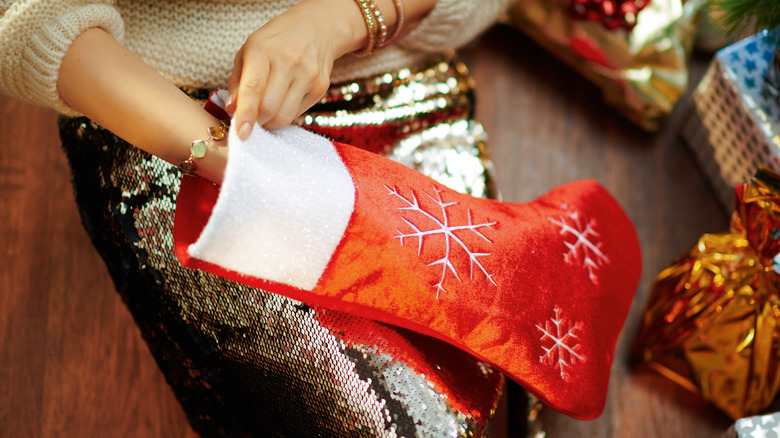 Person in a tan sweater reaching a hand into a red holiday stocking.
