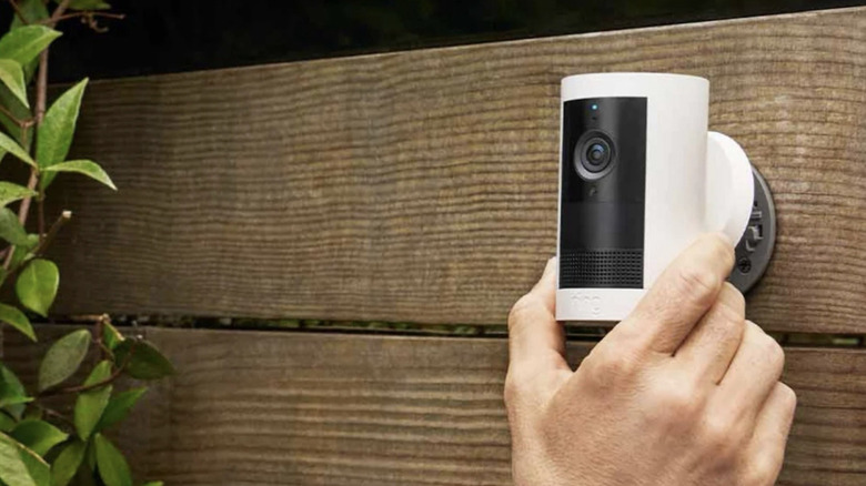 Person adjusting a Ring outdoor camera affixed to a brown fence.