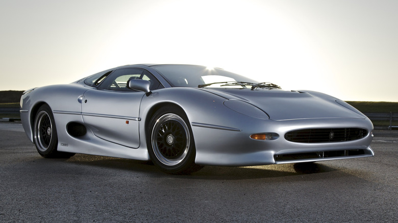 A silver Jaguar XJ220 parked, under a sunrise.